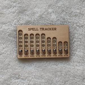 May include: A wooden "Spell Tracker" with engraved text and recessed slots for small metal beads. The tracker has nine columns labeled 1st to 9th, with varying numbers of slots. The text "SPELL TRACKER" is at the top.