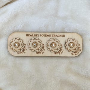 May include: A wooden "Healing Potions Tracker" with four rotating dials labelled "Common", "Greater", "Superior", and "Supreme". Each dial has numbers and a central peg. The text "2 D4+2", "4 D4+4", "6 D4+6", and "10 D4+20" is also visible.