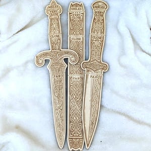 Könnte beinhalten: Drei dekorative Holzdolche mit aufwendigen Schnitzereien. Die Dolche sind hellbraun und tragen die Schriftzüge "MELEE", "VERY CLOSE", "CLOSE" und "FAR". Sie sind vertikal vor einem weißen Hintergrund angeordnet, wodurch ihre Details hervorgehoben werden.