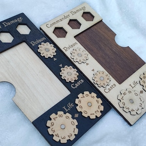 May include: Two wooden game trackers with black and white dials. The dials are labelled "Poison", "Casts", and "Life". The trackers are made of wood and have a natural wood finish.