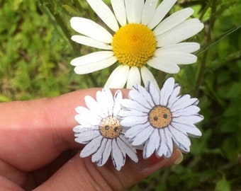 May include: Two white wooden daisy buttons with yellow centers and black outlines. The buttons have a smiley face design with two small black dots for eyes and a yellow smile.