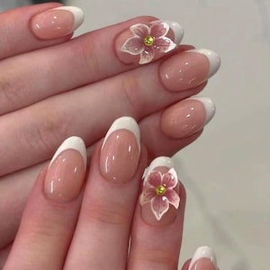 Könnte beinhalten: Manikürte Nägel mit French-Maniküre-Design. Die Nägel haben eine nackte Basis mit weißen Spitzen. Zwei Nägel zeigen eine 3D-rosa Blume mit gelbem Zentrum. Die Nägel sind oval geformt.