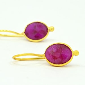 Könnte beinhalten: Ein Paar goldene Ohrringe mit rosafarbenen ovalen Edelsteinen. Die Ohrringe haben ein schlichtes, elegantes Design.
