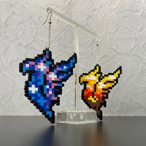 May include: A pair of pixel art earrings featuring a blue and purple phoenix and a yellow and orange phoenix. The earrings are hanging from silver hooks.