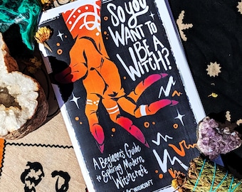 May include: A book titled So You Want To Be A Witch? A Beginner's Guide to Exploring Modern Witchcraft by Wit Will & Witchcraft. The cover features a stylized orange and red hand illustration against a black background with white text.