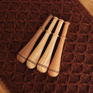May include: Four wooden knitting needles with black trim, arranged on a brown knitted fabric.