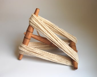 May include: A wooden yarn swift with a natural finish, holding a skein of white yarn.