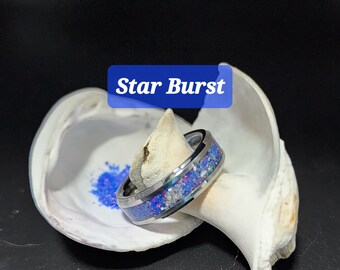 May include: A silver-toned ring with a band of blue and purple iridescent material. The ring is set against a white seashell with a blue powder. The text "Star Burst" is in a blue box.