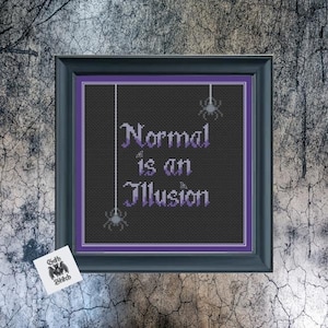 May include: A black framed cross-stitch with purple embroidery. The cross-stitch features the text "Normal is an Illusion" with small spider silhouettes hanging from the top.