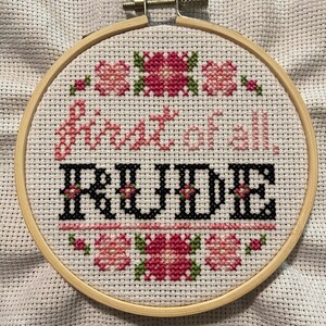 May include: A white embroidery hoop with a pink and green floral design and the text "Don't be so" followed by the word "RUDE" in black.