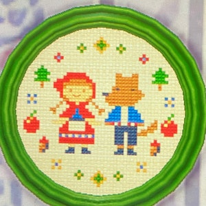 May include: A green framed embroidery hoop with a white background featuring a red-hooded girl and a wolf in blue clothing. The embroidery includes red apples, green trees, and yellow flowers.