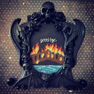 May include: A black ornate frame with a dragon design and a cross-stitch image of a burning building with the text "good-bye."