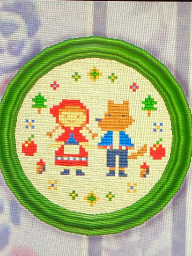 May include: A framed cross-stitch embroidery depicting a red-hooded girl and a wolf in a forest setting. The embroidery features a white background with red, blue, and green accents.