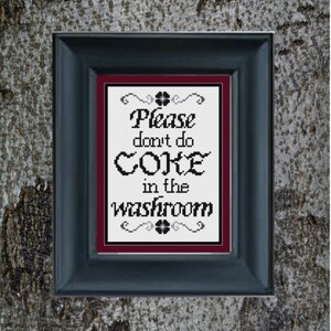 May include: A framed sign with a white background and black text that reads "Please don't do coke in the washroom". The frame is black with a maroon mat.