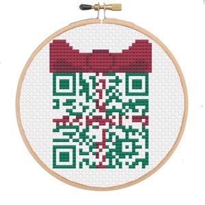 May include: A green and red cross-stitch pattern of a QR code with a red bow on top. The pattern is framed in a wooden embroidery hoop.