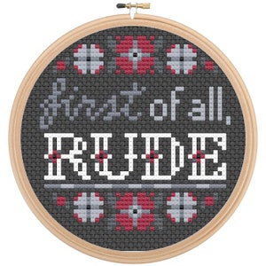 May include: A black and white cross-stitch embroidery hoop with the text "First of all, rude." in gray and white lettering. The hoop is decorated with a red and white geometric pattern.