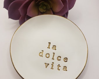 May include: White ceramic trinket dish with a gold rim and the words "la dolce vita" written in gold lettering.