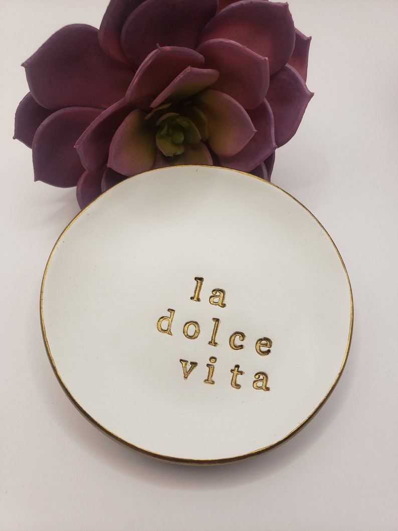 White trinket dish with a gold rim and the words "la dolce vita" written in gold lettering.  Would make a perfect gift for an Italian Wedding Engagement Gift.