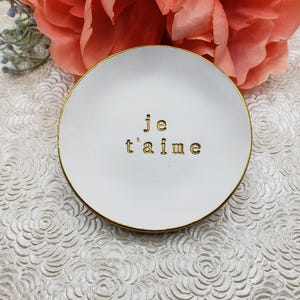 May include: White ceramic trinket dish with a gold rim and the words "je t'aime" written in gold lettering.