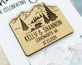 May include: A wooden magnet with a mountain and bear design. The magnet is engraved with the names "Kelly & Shannon", the location "Leavenworth, WA", and the date "07.23.2024". The magnet is light brown with dark brown engraved details.