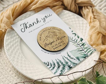 May include: A white card with a watercolor fern design and the words "Thank you" in script. A wooden magnet with the text "Our adventure begins" and the names "Harper & Lucas" is on the card. The magnet also includes the date "10.10.2023" and the city "Denver CO".