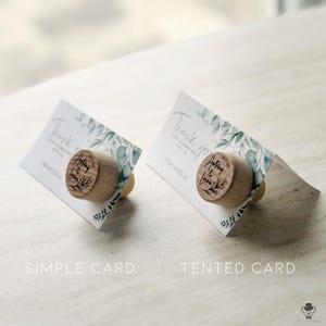 May include: Two wedding favour cards with a wooden bottle stopper featuring the text "Anthony & Laura" and the date "18.11.2022". The card on the left is a simple card, while the card on the right is tented.