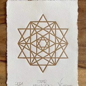 Può includere: Una stampa geometrica dorata di un esagono stellato su sfondo bianco. La stampa è firmata "STAR HEXAGON" e "V.COESSENS".