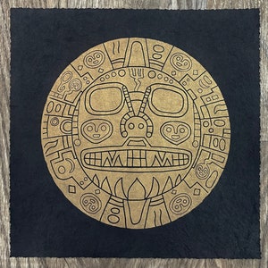 Peut inclure: Un motif circulaire doré avec des motifs complexes et un visage stylisé sur un fond noir. Le motif ressemble à un symbole traditionnel du soleil ou de la lune.