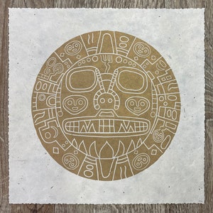 Peut inclure: Une impression sur papier blanc avec un motif circulaire brun. Le cercle présente un visage stylisé avec des motifs et des lignes géométriques.