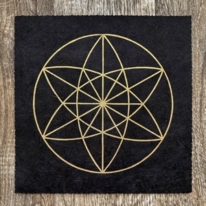 May include: A black felt mat with a gold geometric design. The design is a circle with a star inside, and the star is made up of many lines.