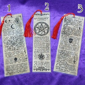 May include: Three bookmarks with black and white illustrations of symbols and text on a parchment-like background. The bookmarks have red tassels.