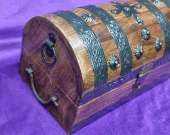 Può includere: Uno scrigno del tesoro in legno con un coperchio curvo e dettagli in metallo. Lo scrigno ha una maniglia in metallo nero e una chiusura in metallo decorativa.