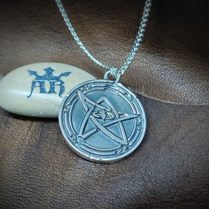 May include: Silver pendant necklace featuring a five-pointed star with an eye in the center. The star is surrounded by a circle with a decorative border.