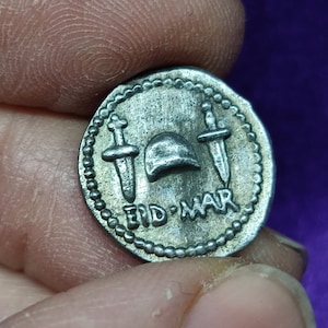 May include: Silver coin with a raised design of two swords crossed over a helmet with the inscription "EID-MAR".