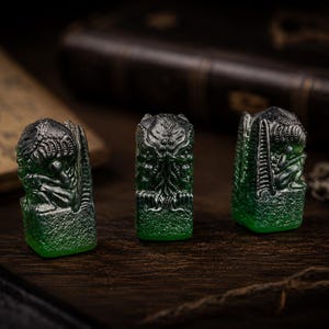 May include: Three small, translucent green resin figurines with dark metallic highlights. Each piece features a detailed, sculpted creature with tentacled facial features and textured wings, standing on a rectangular base with a rough, stone-like finish.