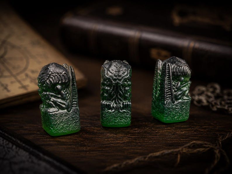 May include: Three small, translucent green resin figurines with dark metallic highlights. Each piece features a detailed, sculpted creature with tentacled facial features and textured wings, standing on a rectangular base with a rough, stone-like finish.