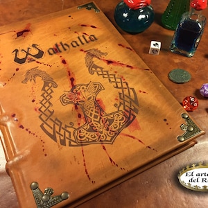 May include: A brown leather-bound journal with a gold embossed design of a hammer and a dragon. The journal is titled "Valhalla" and has red splatter paint on the cover.