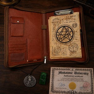 May include: A brown leather portfolio containing aged parchment paper with black occult symbols and a metal clip. Included are a silver-toned octopus pendant on a black cord, a small green carved figurine, and a Miskatonic University certificate.