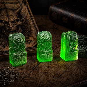 May include: Three translucent, vibrant green resin figurines, each featuring a detailed, tentacled creature design. These small, upright sculptures have a textured base and a smooth, glossy finish, showcasing intricate carvings of a mythical entity.