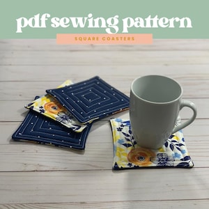 Könnte beinhalten: Vier quadratische Stoffuntersetzer mit einem blauen und weißen Blumenmuster. Die Untersetzer sind gesteppt und haben einen weißen Hintergrund mit blauen und gelben Blumendesigns. Eine weiße Tasse steht auf einem der Untersetzer.