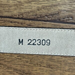 Puede incluir: Primer plano de una etiqueta de cuero beige con costuras negras y el texto "M 22309" impreso en ella.