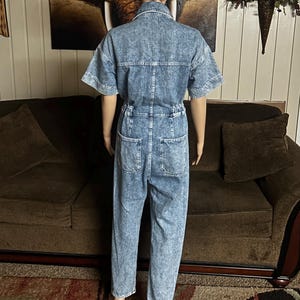 Peut inclure: Une combinaison en jean bleu clair &agrave; manches courtes et &agrave; fermeture boutonn&eacute;e sur le devant. La combinaison a une coupe d&eacute;contract&eacute;e et un aspect l&eacute;g&egrave;rement d&eacute;lav&eacute;.