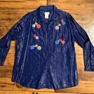 May include: A navy blue long-sleeved button-down shirt with a silver shimmer. The shirt is decorated with colorful embroidered ornaments.