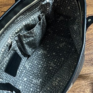 May include: Black leather tote bag with a white and gray polka dot lining. The bag has a zipper closure and multiple interior pockets.