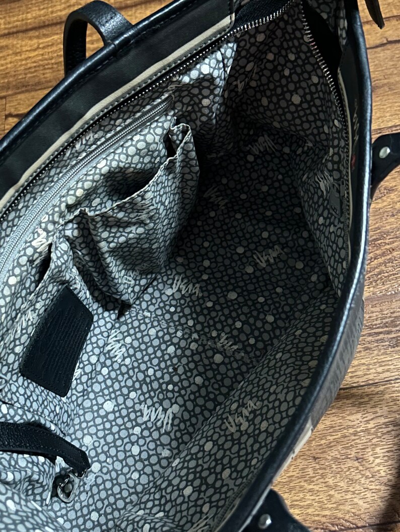 May include: Black leather tote bag with a white and gray polka dot lining. The bag has a zipper closure and multiple interior pockets.