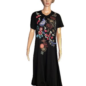 Puede incluir: Un vestido midi negro de manga corta con cuello redondo y dobladillo con volantes. La parte delantera del vestido est&aacute; decorada con bordados coloridos que representan un p&aacute;jaro azul, fresas rojas y varios motivos florales en tonos naranja, amarillo y blanco.
