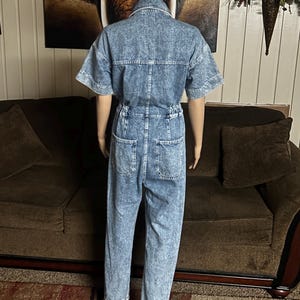 Peut inclure: Une combinaison en jean bleu clair &agrave; manches courtes et &agrave; fermeture boutonn&eacute;e. La combinaison a une coupe d&eacute;contract&eacute;e et un aspect l&eacute;g&egrave;rement d&eacute;lav&eacute;.