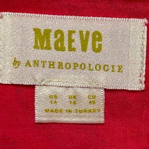 May include: White tag with gold text that reads "Maeve by Anthropologie" and size information: US 14, UK 18, EU 44. The tag is on a red fabric background.