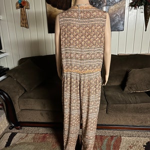 May include: A sleeveless jumpsuit with a geometric pattern in shades of brown, orange, and white. The jumpsuit has a wide leg and a drawstring waist.