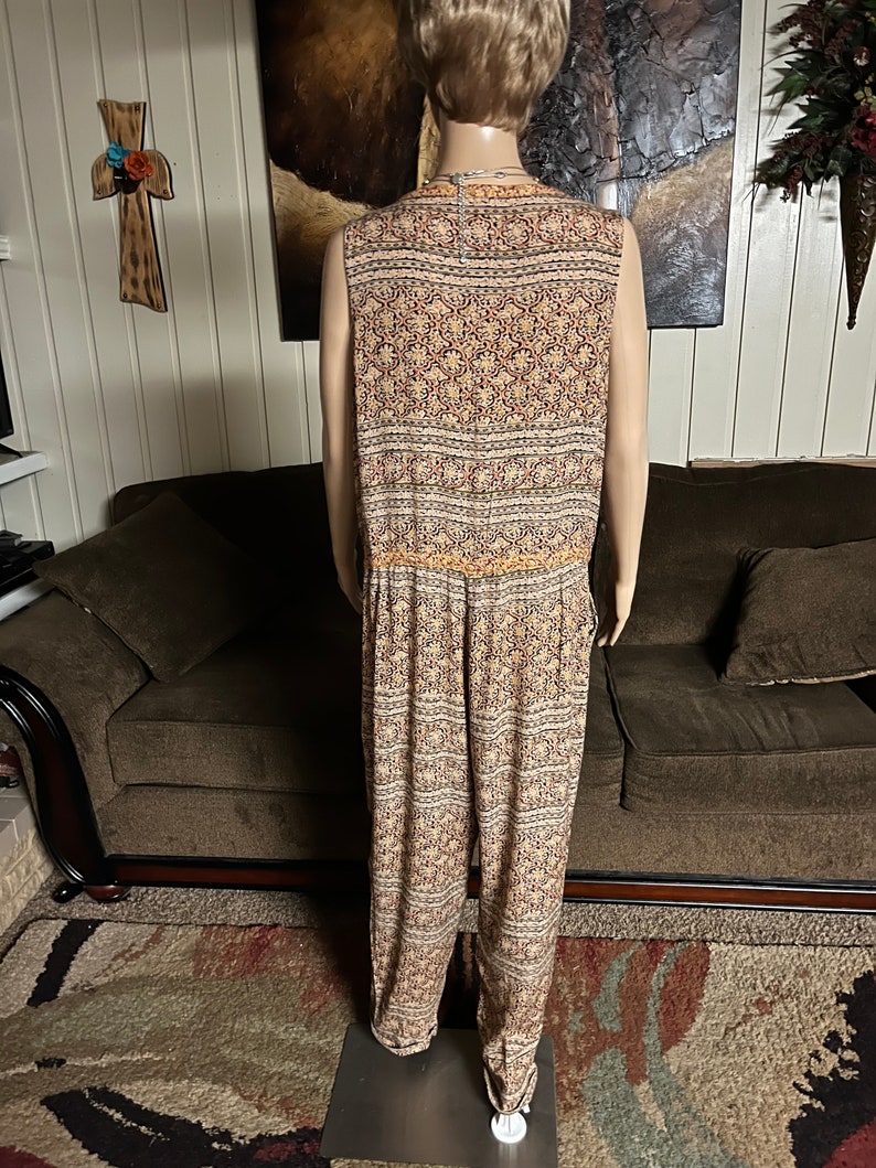 May include: A sleeveless jumpsuit with a geometric pattern in shades of brown, orange, and white. The jumpsuit has a wide leg and a drawstring waist.